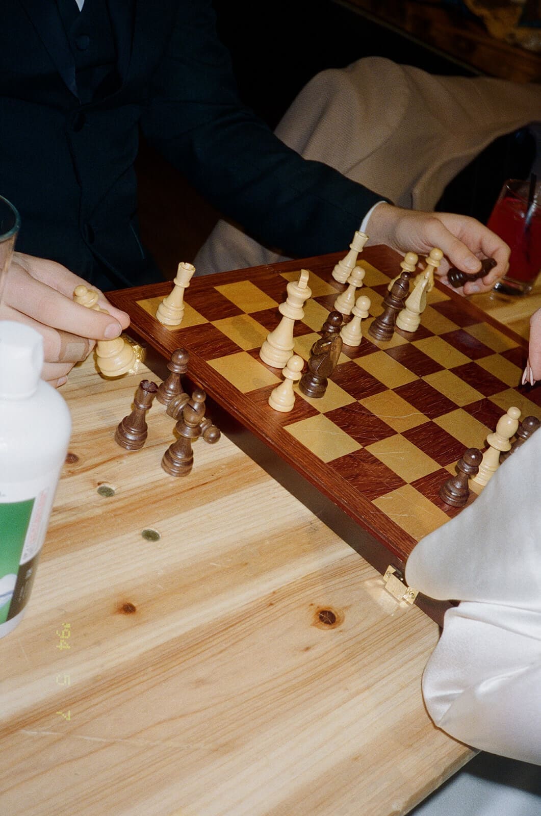 Candid wedding photos of guests playing chess at a wooden table during the reception.