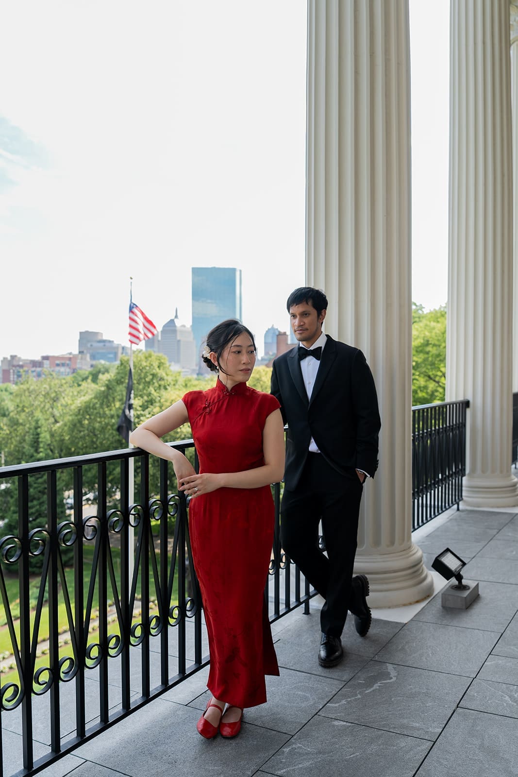 Couple poses on a columned balcony overlooking Boston after their City Hall ceremony.