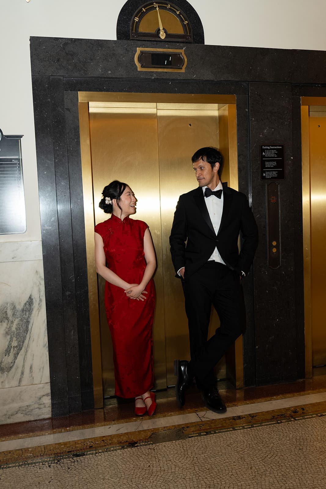 Newlyweds smile at each other beside the gold elevators inside Boston City Hall.