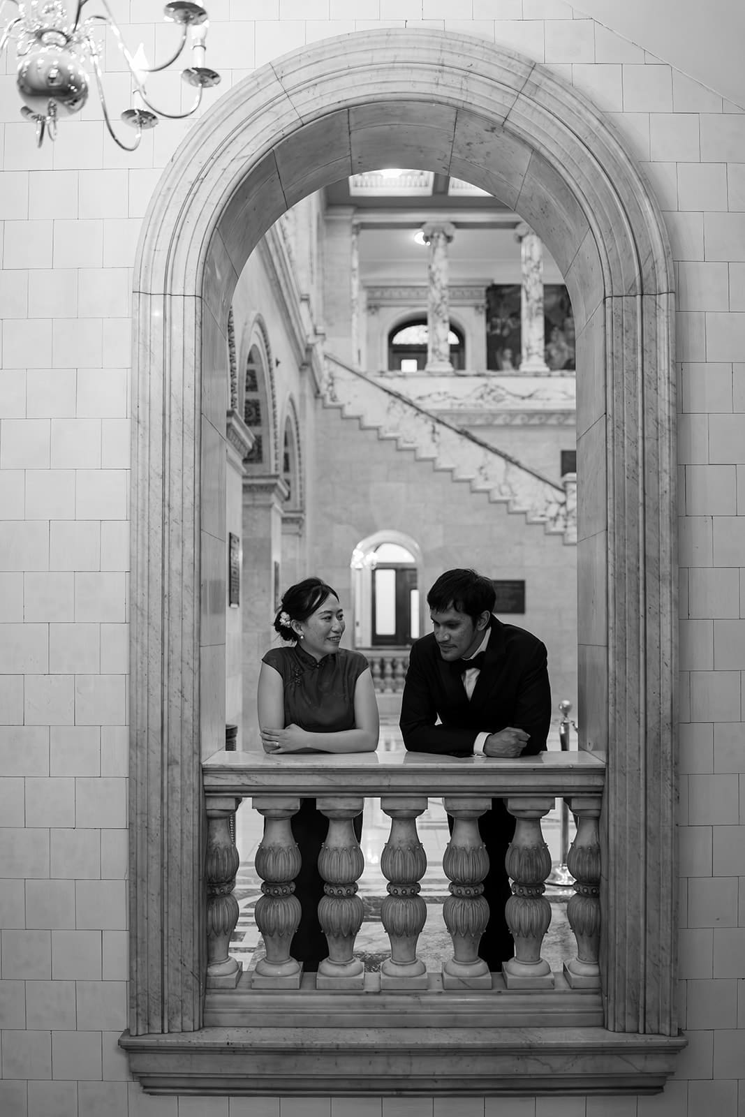 Black-and-white portrait of a couple framed by an ornate arch inside Boston City Hall.