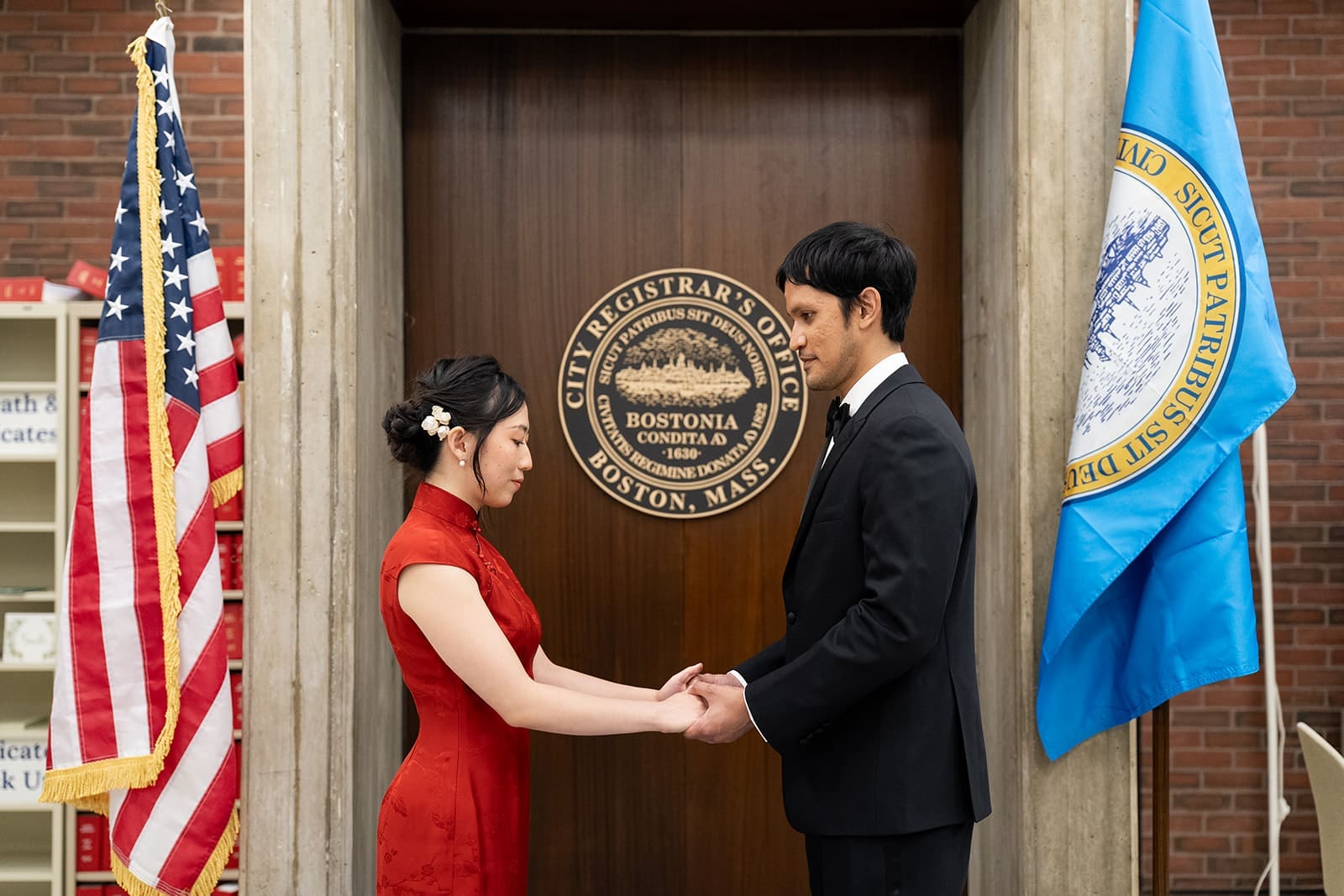 Couple holds hands between American and Massachusetts flags during their Boston City Hall ceremony.