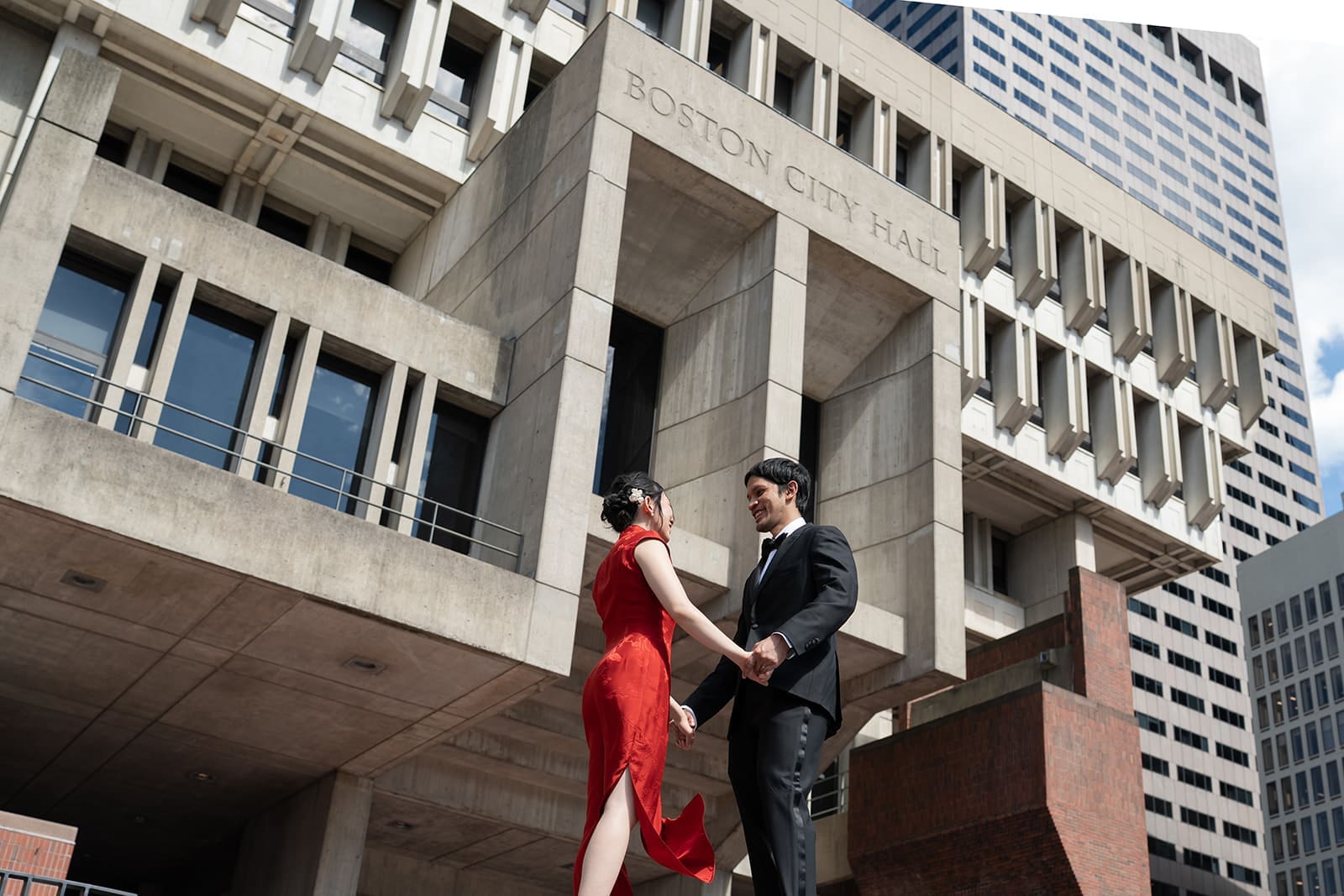 Couple holds hands in front of Boston City Hall after their wedding ceremony.