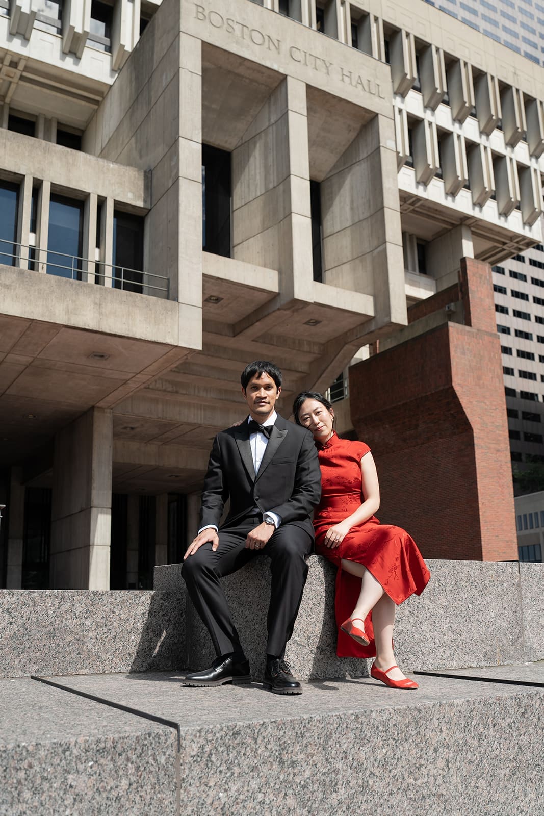 Newlyweds sit together beneath the Boston City Hall sign after their wedding ceremony.