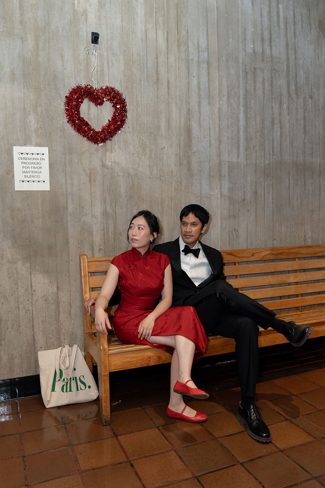 Couple relaxes together on a wooden bench inside Boston City Hall beneath a heart decoration.