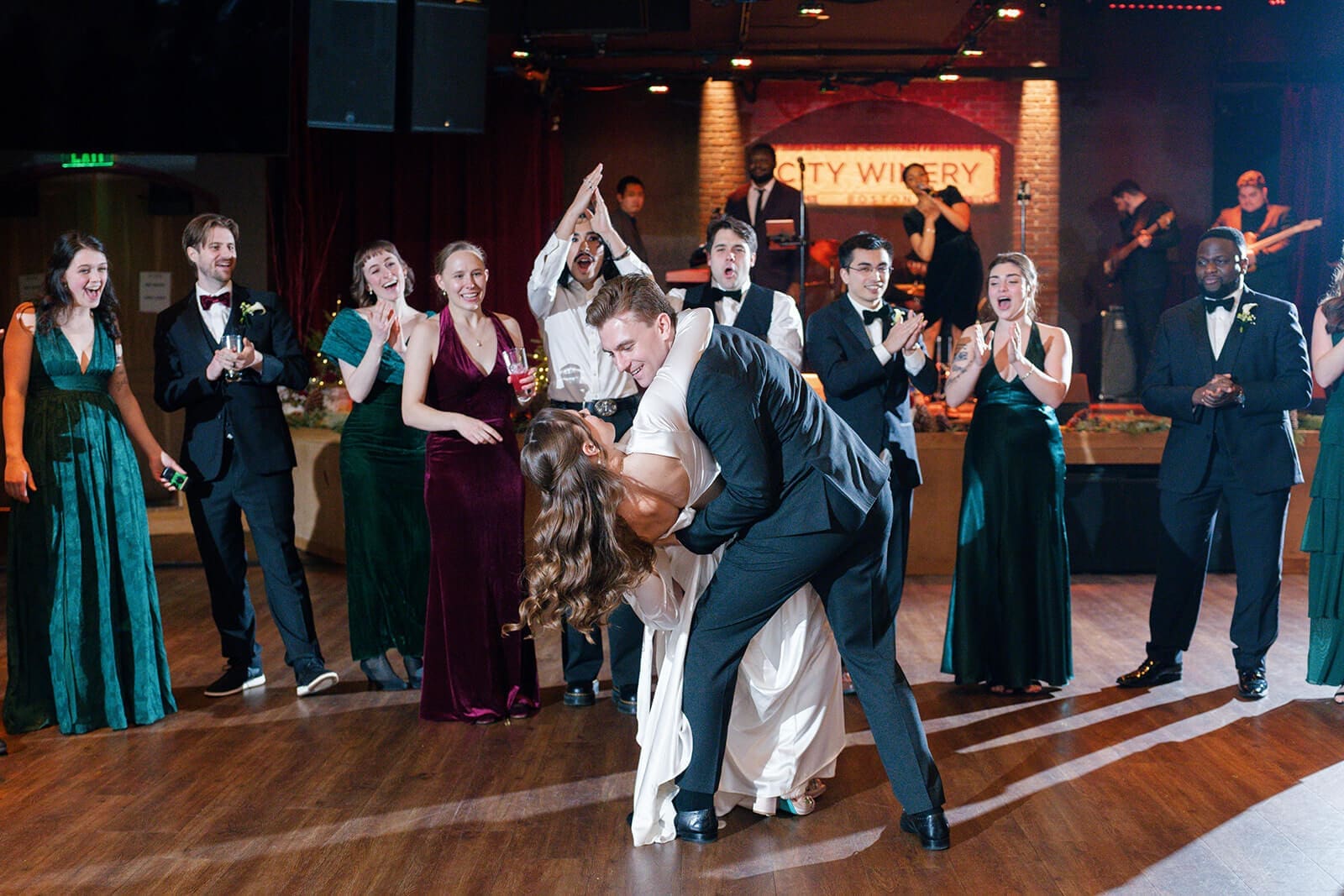 Candid wedding photos of the groom dipping and kissing the bride as their wedding party cheers.