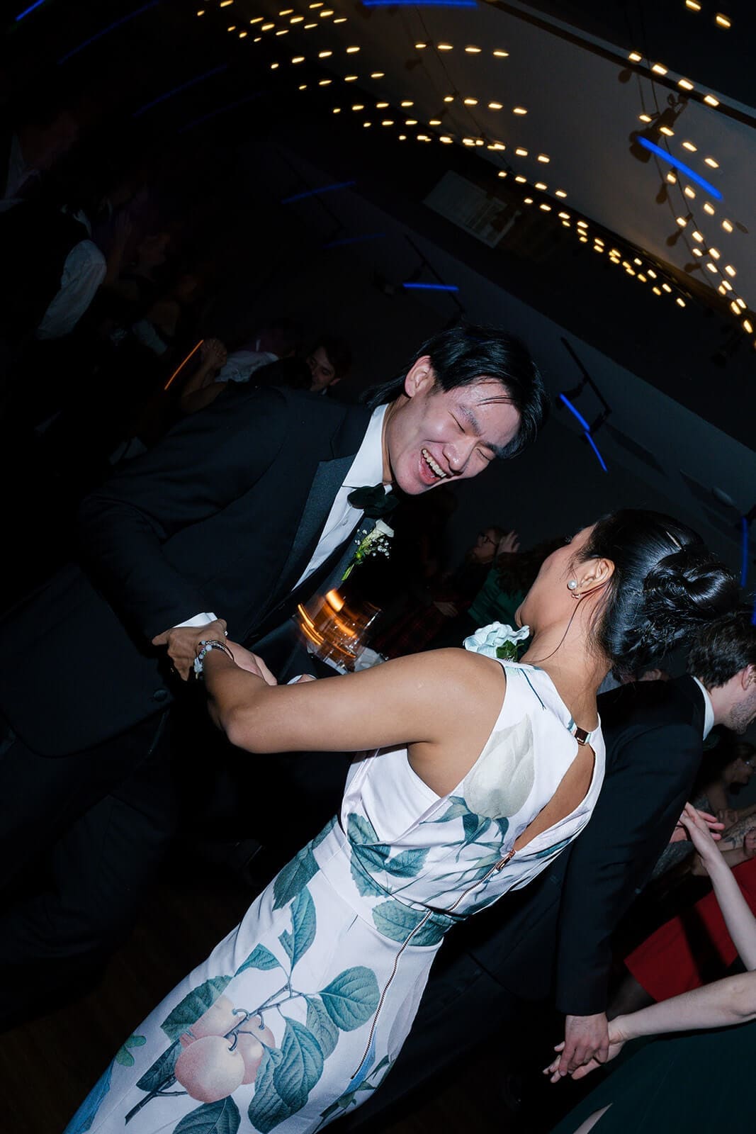 Candid wedding photos of two wedding guests laughing together on the crowded reception dance floor.