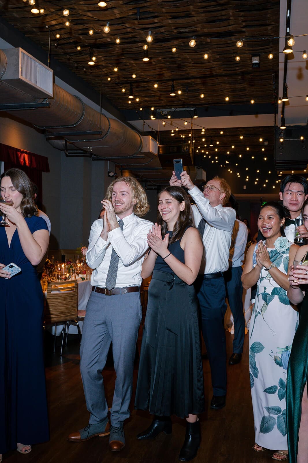 Candid wedding photos of wedding guests smiling and applauding beside the dance floor.