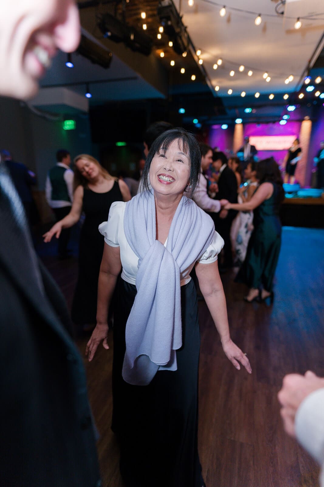Candid wedding photos of a smiling guest dancing with friends beneath glowing string lights.