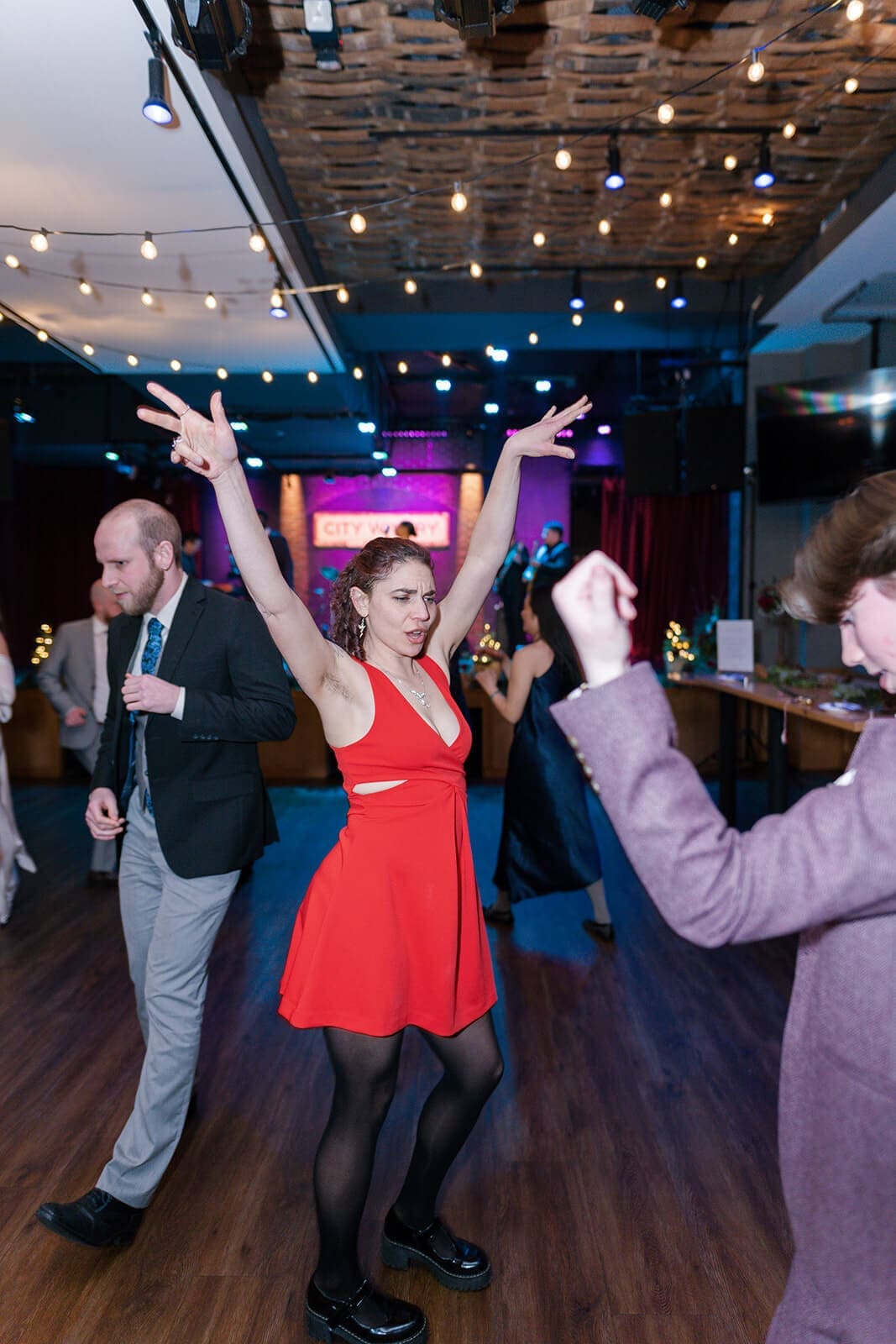 Candid wedding photos of a guest in a red dress dancing with both hands raised.