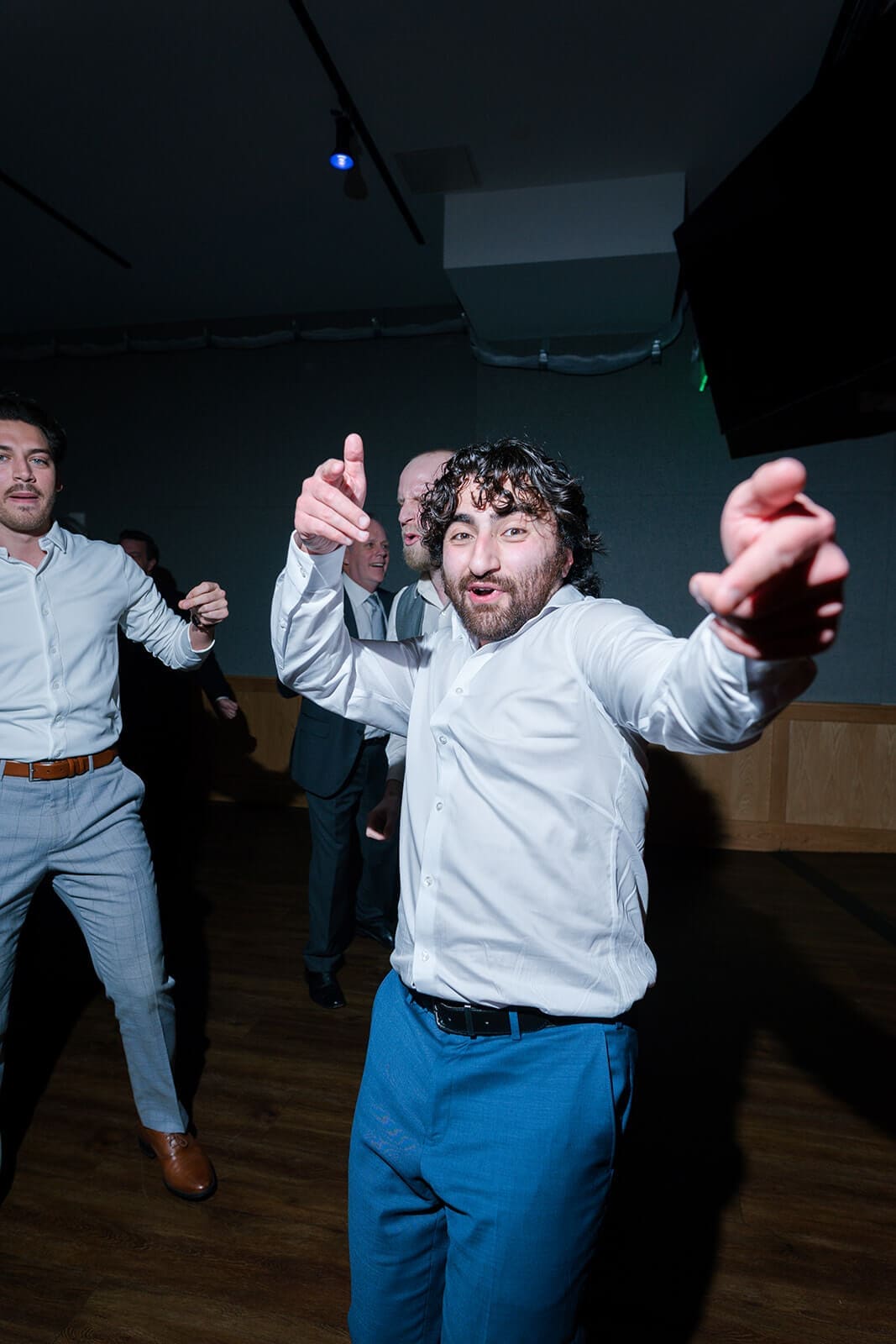 Candid wedding photos of a guest pointing toward the camera while dancing at the reception.