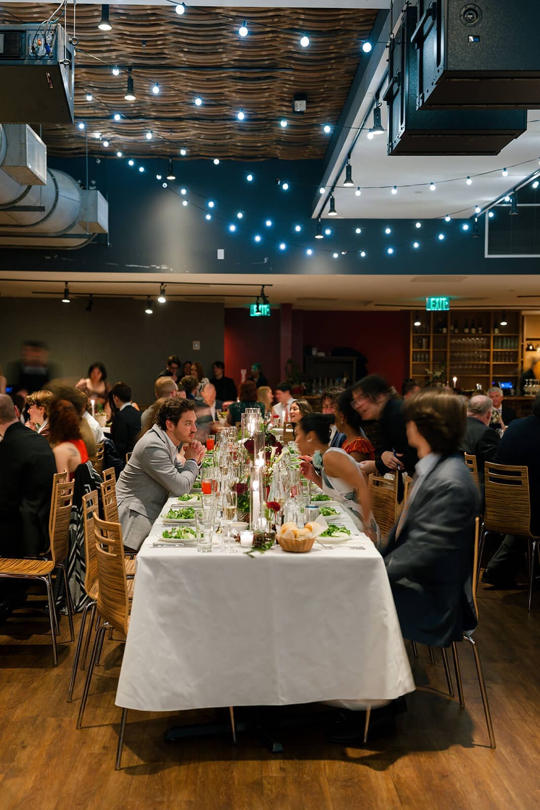Candid wedding photos of guests gathered around long reception tables beneath warm string lights.