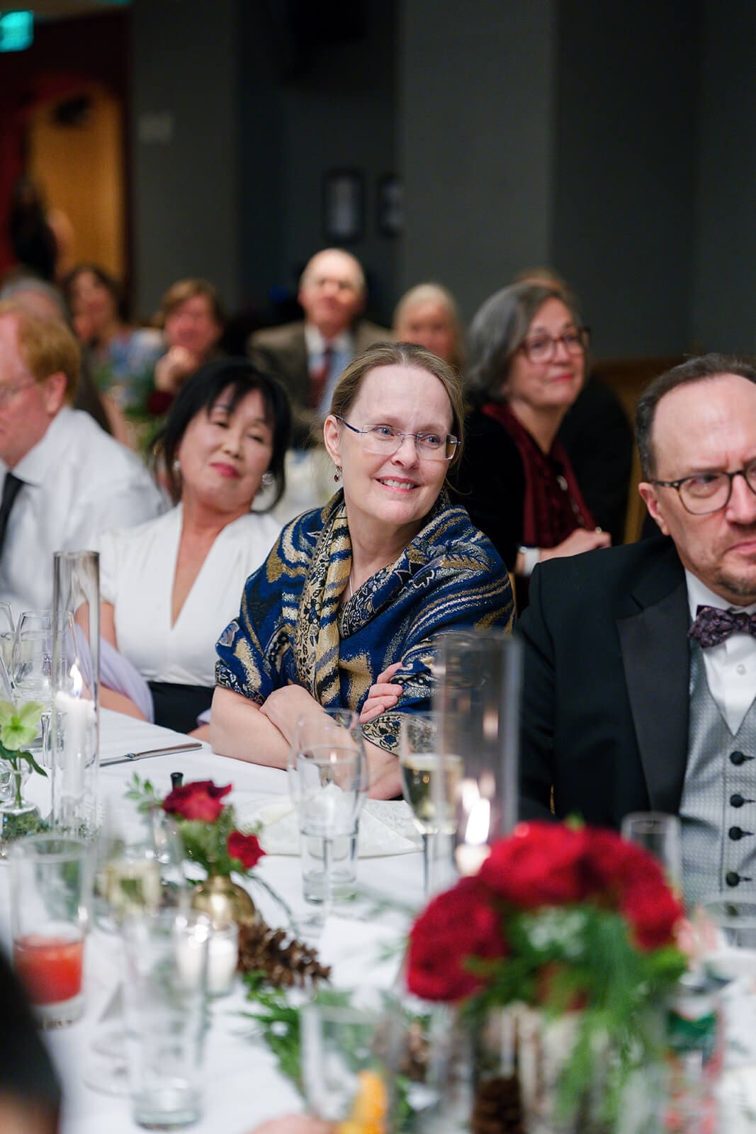 Candid wedding photos of seated guests smiling and listening during the wedding reception.