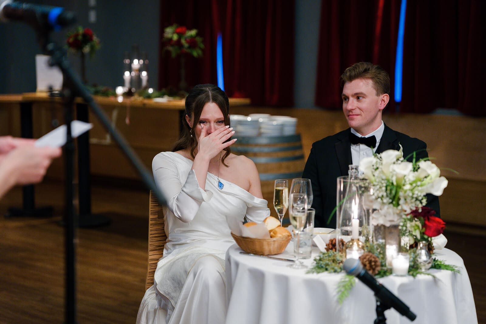Candid wedding photos of the bride wiping away tears as the groom smiles beside her.