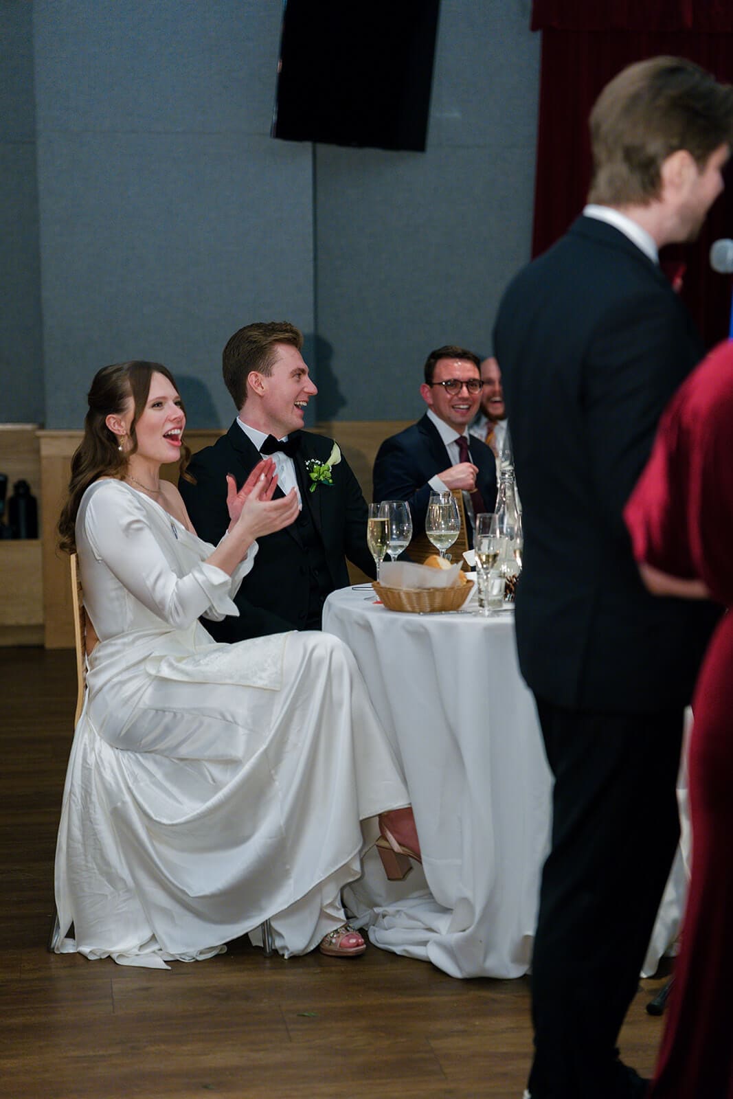 Candid wedding photos of the newlyweds clapping and laughing while listening to a toast.
