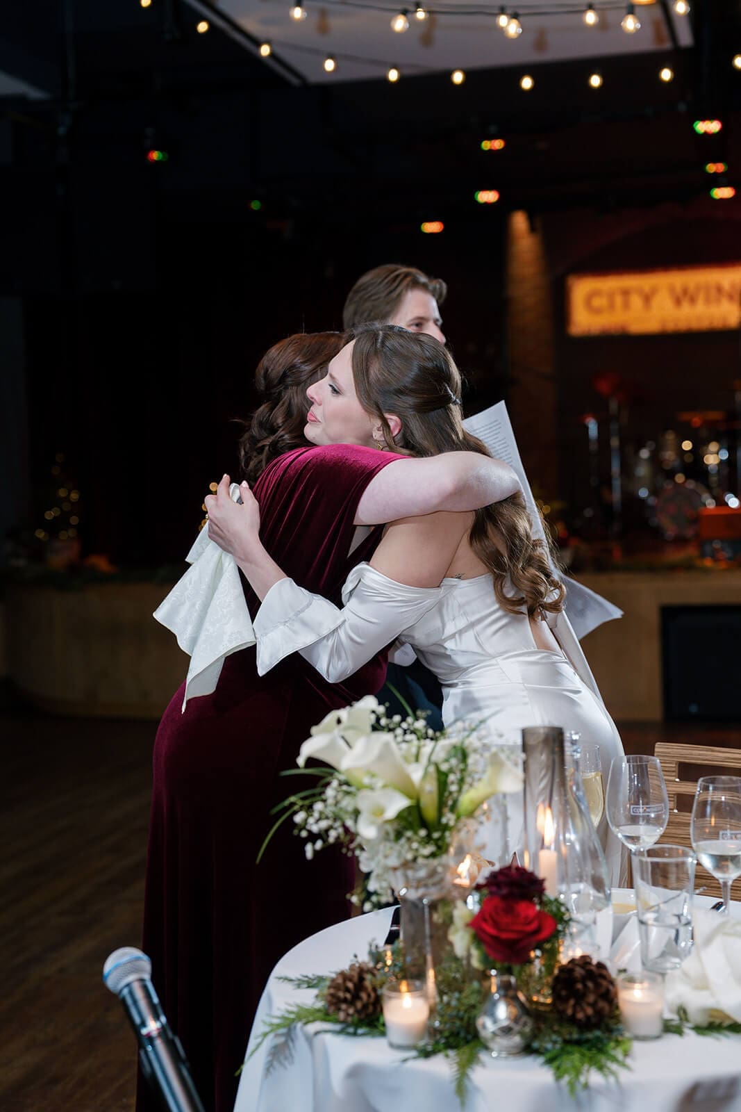 Candid wedding photos of the bride hugging her bridesmaid beside the decorated sweetheart table.