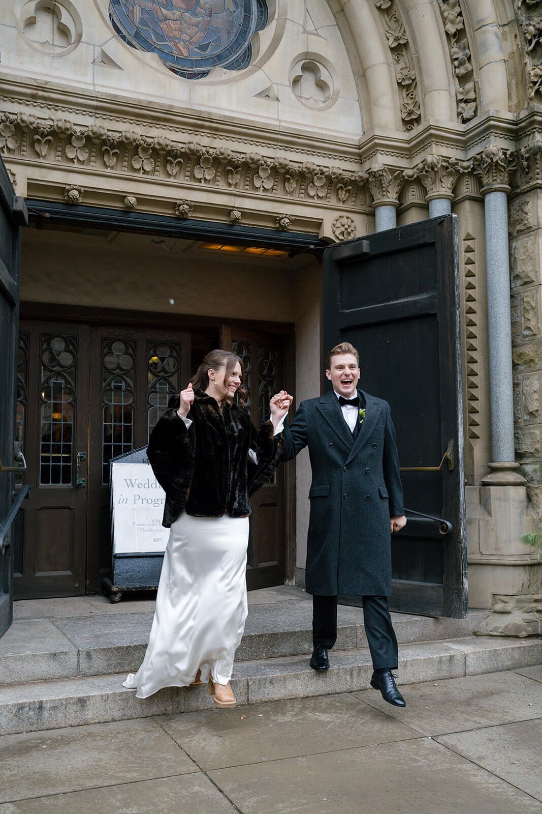 Bride and groom playfully celebrating outside the ornate entrance of their historic Boston church.