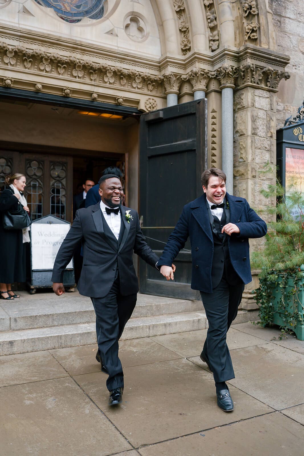 Groomsmen laughing as they walk out of a historic Boston church following the wedding ceremony.