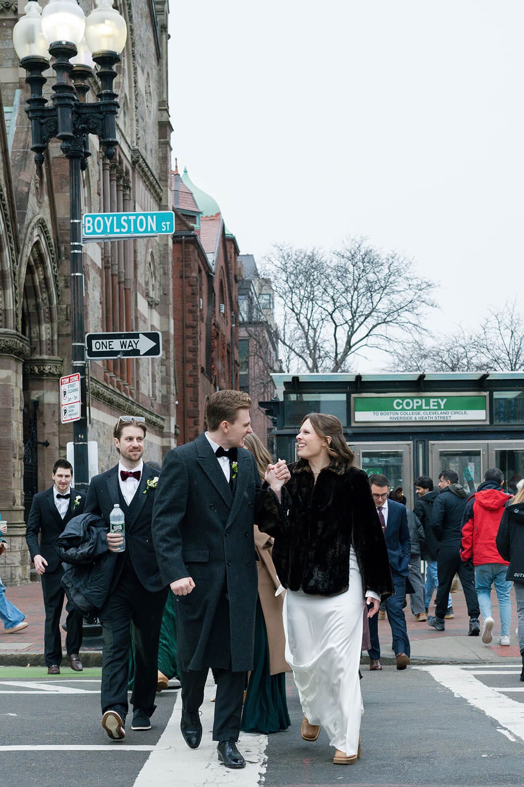 Bride and groom walking across Boylston Street with members of their wedding party behind them.