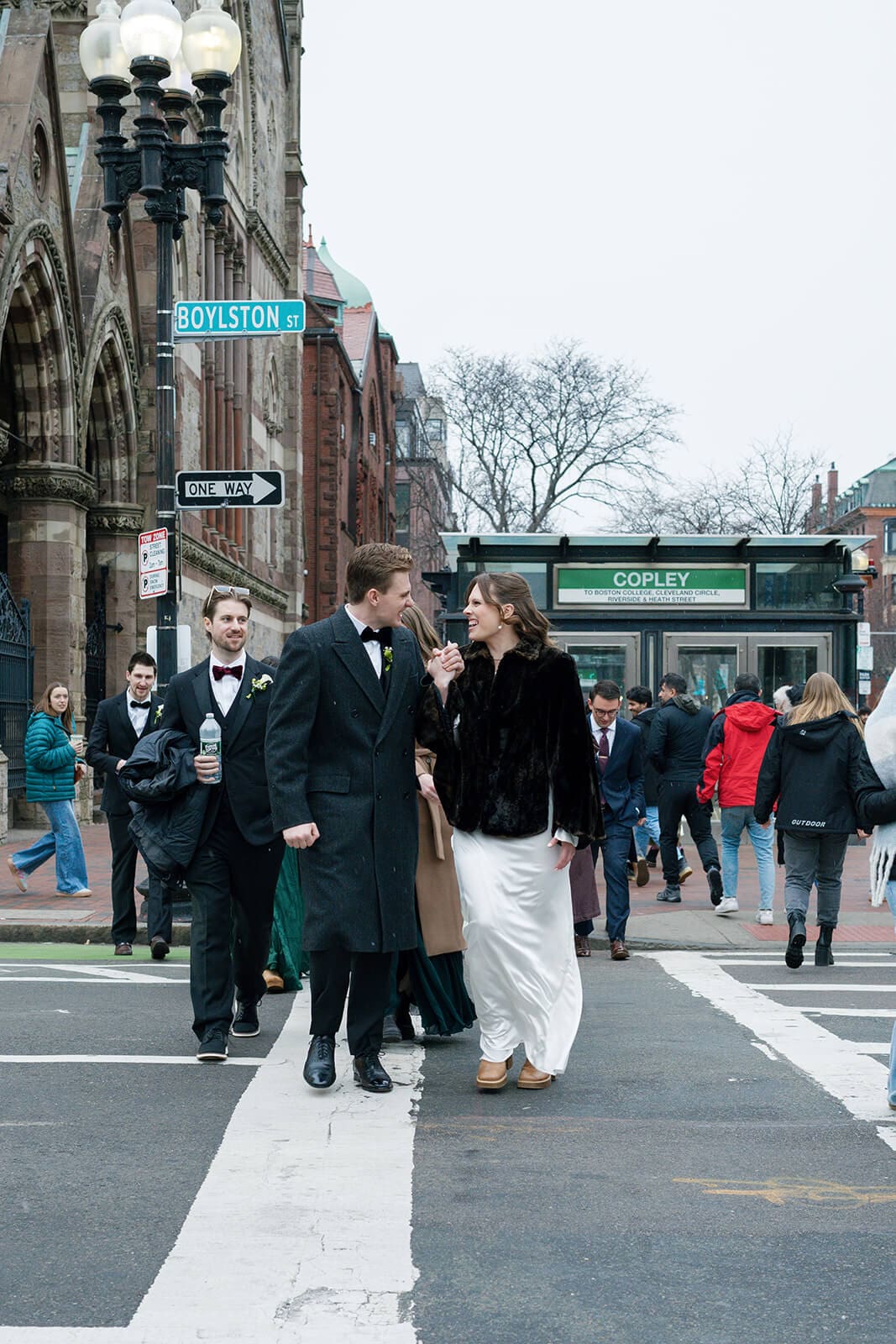 Bride and groom walking across a Boston crosswalk with their wedding party following behind them.