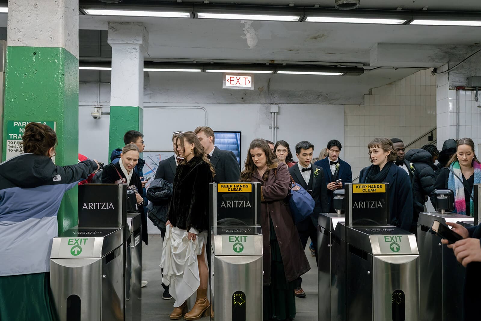 Bride and groom walking through the turnstiles at Copley station surrounded by Boston commuters.