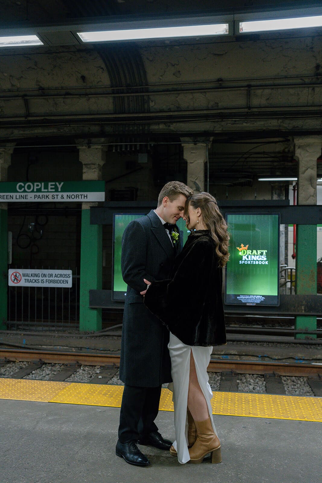 Newlyweds kissing on the subway platform beneath the Copley station sign.