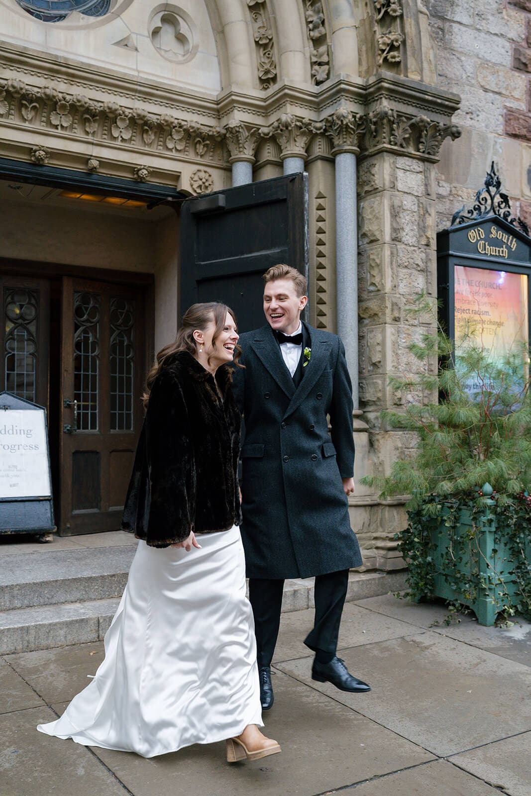 Bride and groom laughing as they walk away from their Boston church wedding ceremony.