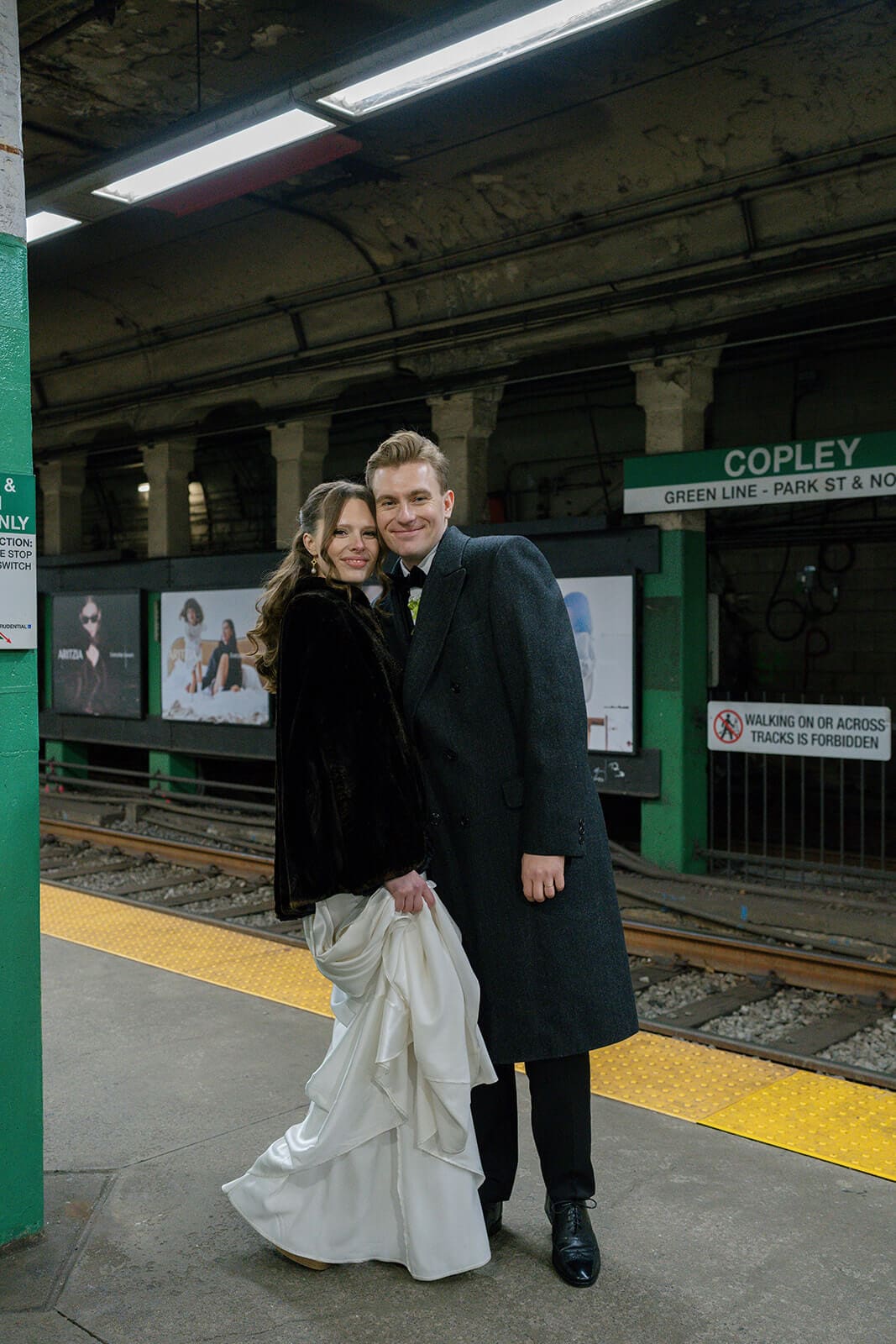 Bride and groom standing together on the subway platform at Copley station in Boston.