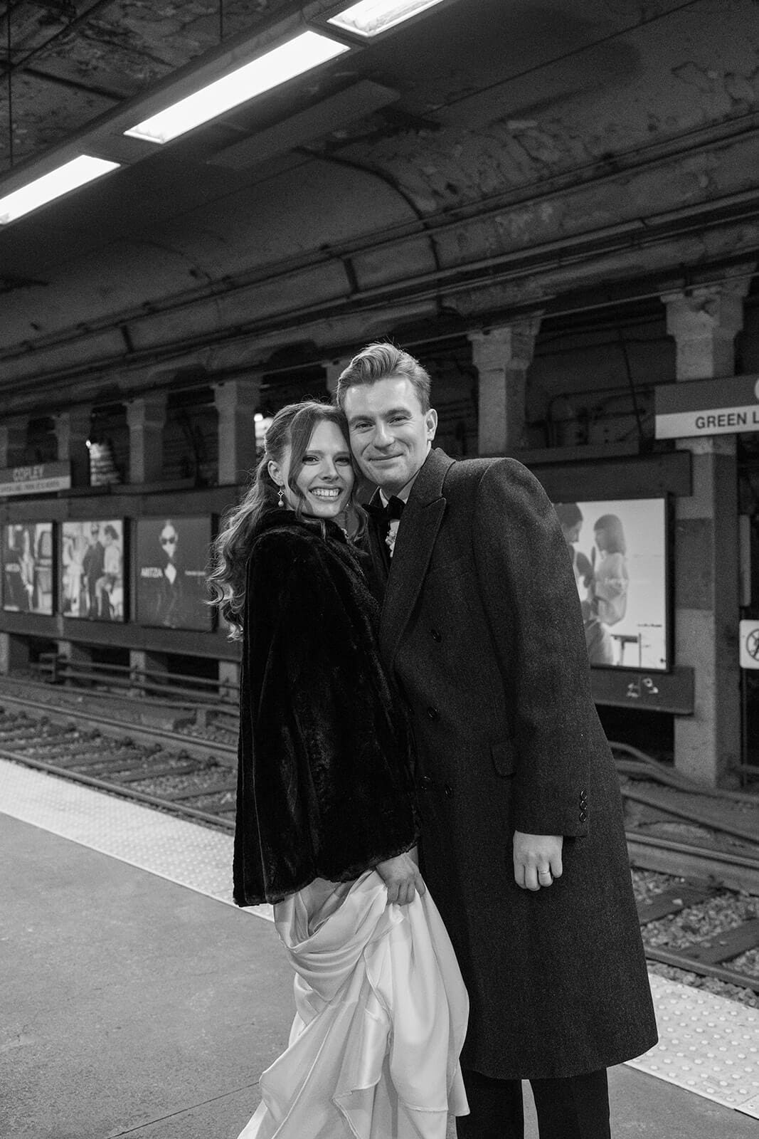 Black and white portrait of a bride and groom standing together on the Copley Green Line platform.