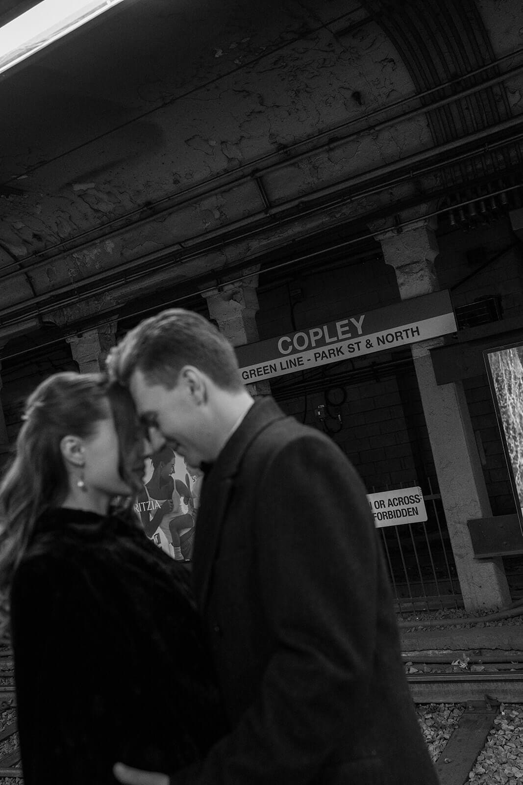 Black and white portrait of newlyweds standing close together on the Copley Green Line platform.