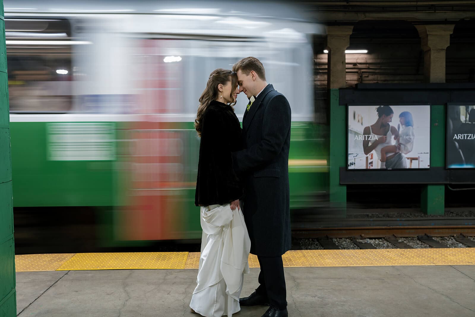 Bride and groom standing forehead to forehead on a Boston subway platform as a Green Line train blurs behind them.