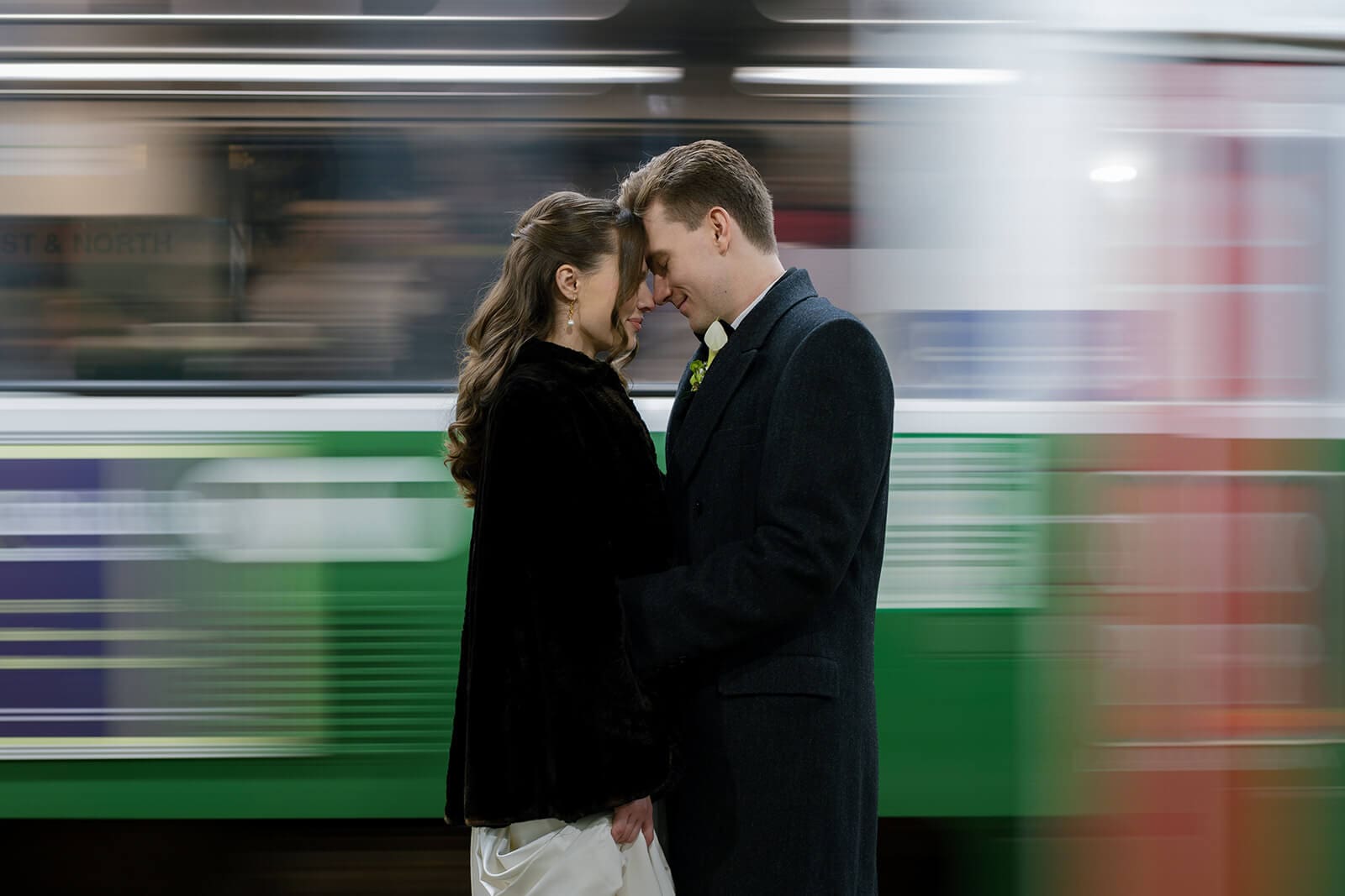 Bride and groom standing close on a Boston subway platform as a Green Line train rushes behind them.