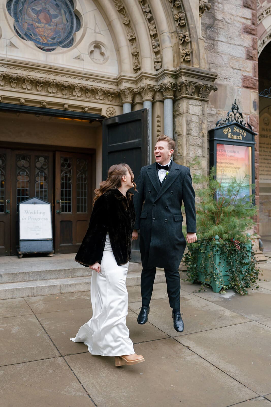 Bride and groom laughing outside a historic Boston church after their wedding ceremony.