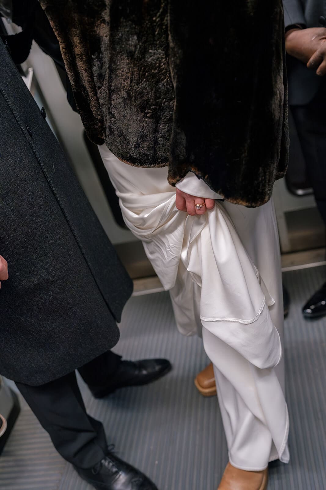 Close-up of a bride and groom holding hands while riding public transportation through Boston.