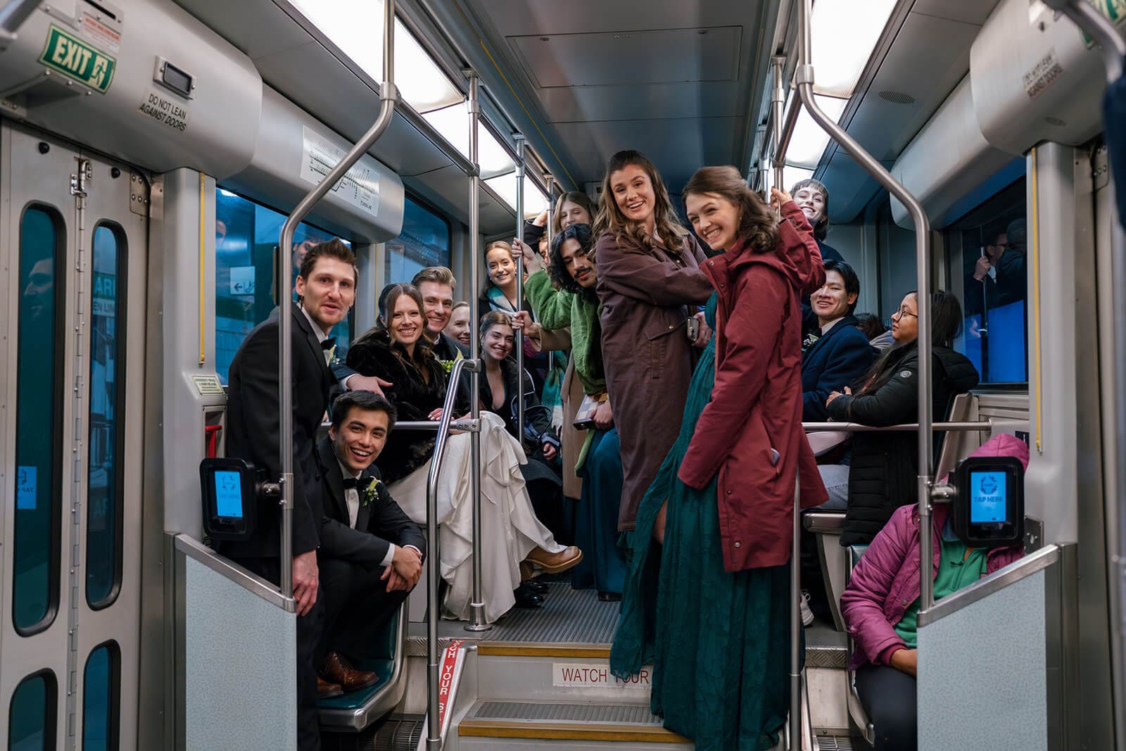 Wedding party laughing together inside a Boston MBTA train during the trip to the reception.