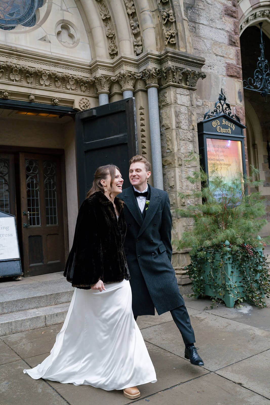 Newlyweds laughing together outside a Boston church immediately after their wedding ceremony.