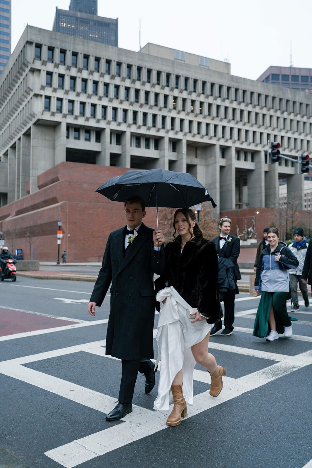 Bride and groom walking through downtown Boston beneath an umbrella on their rainy wedding day.