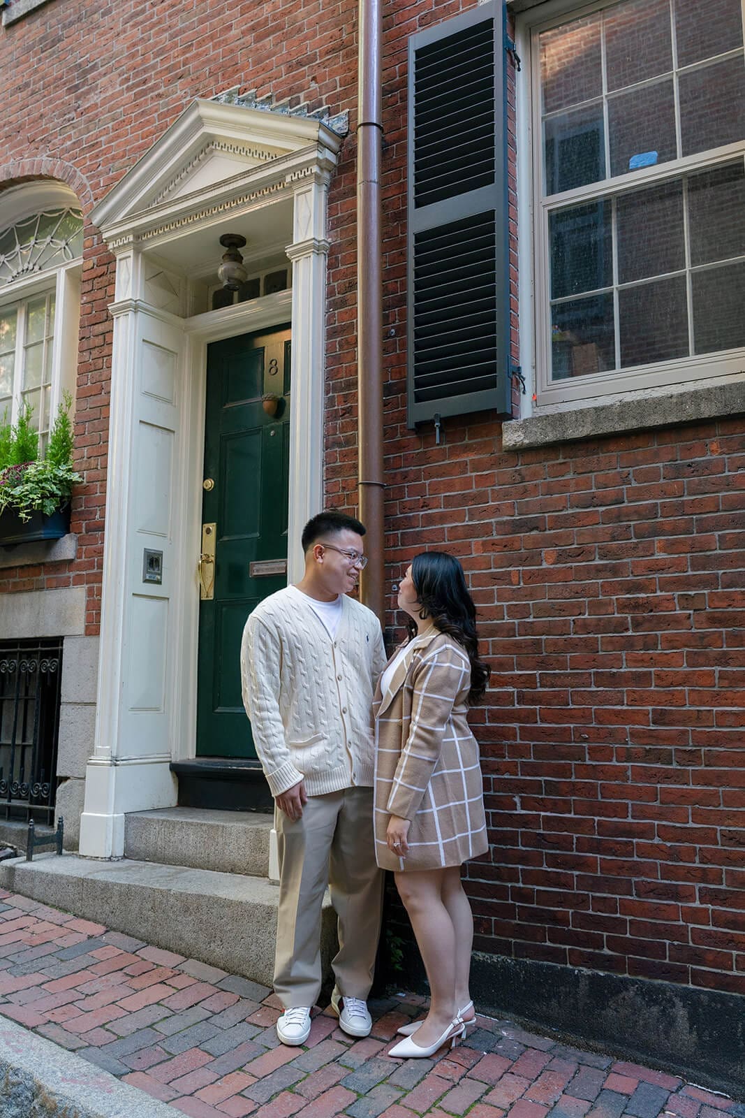 Couple standing close and facing each other beside the doorway of a historic brick Beacon Hill home.