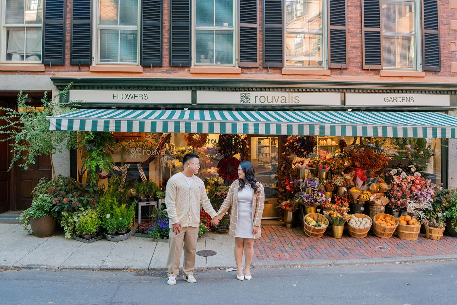 Wide portrait of a couple holding hands in front of Rouvalis Flowers on Beacon Hill in Boston.