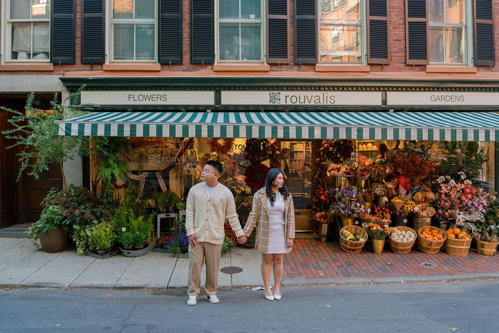Wide portrait of a couple holding hands in the street in front of the colorful displays at Rouvalis Flowers on Beacon Hill.