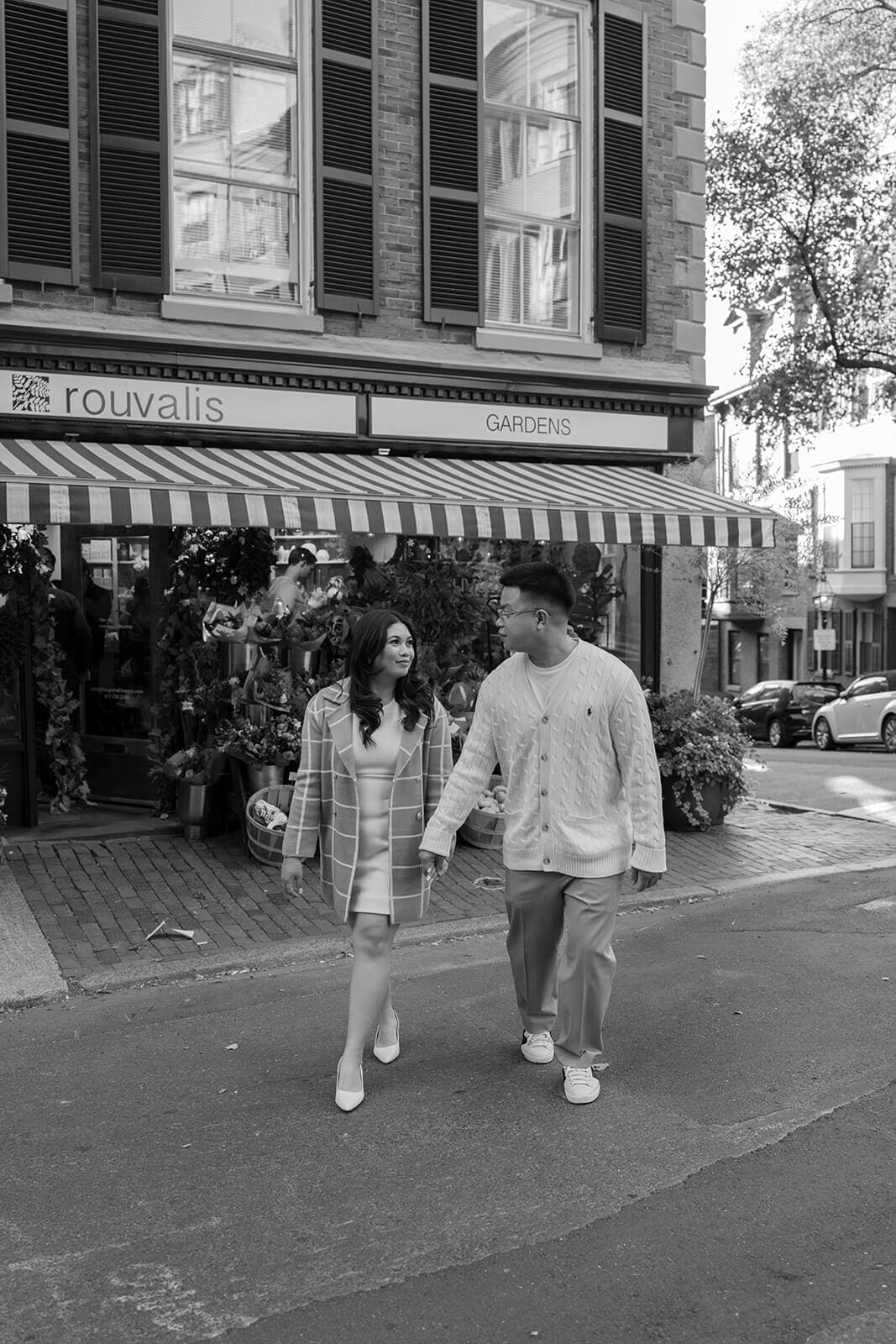Black-and-white photograph of a couple walking together in the street outside a Beacon Hill flower shop.