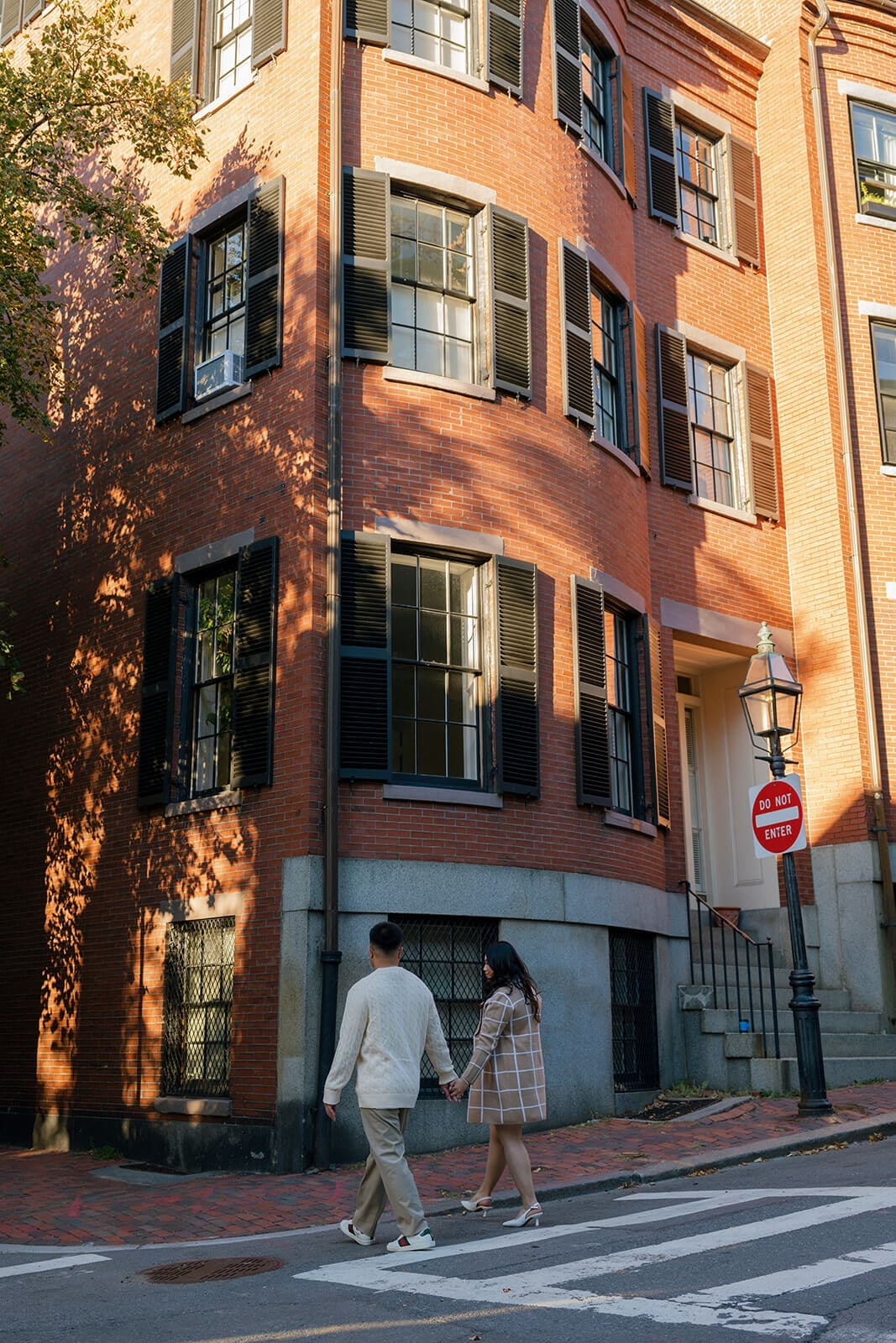 Couple walking away together around the corner of a sunlit red brick building on Beacon Hill.