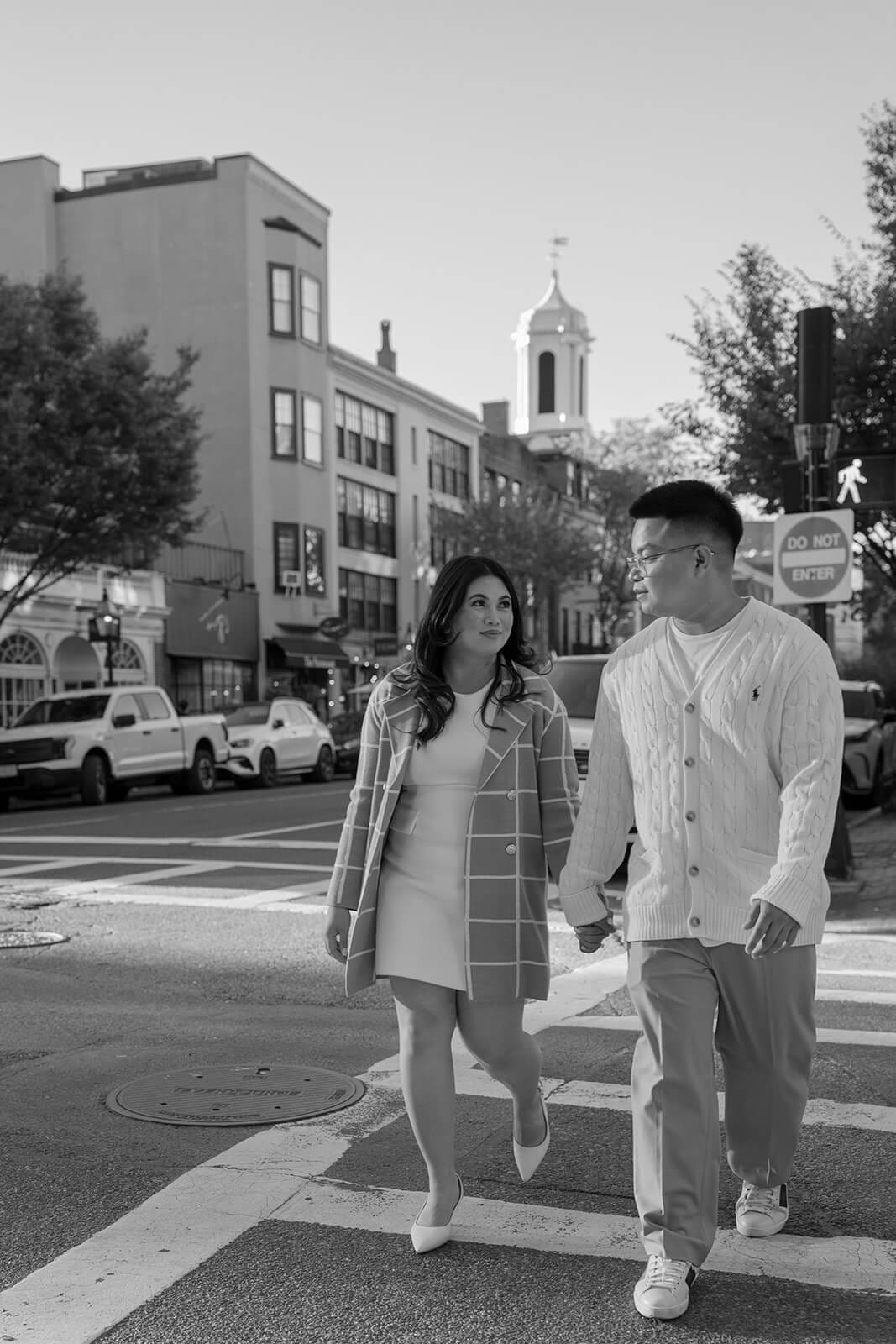 Black-and-white photograph of a couple holding hands while crossing a Boston city street.