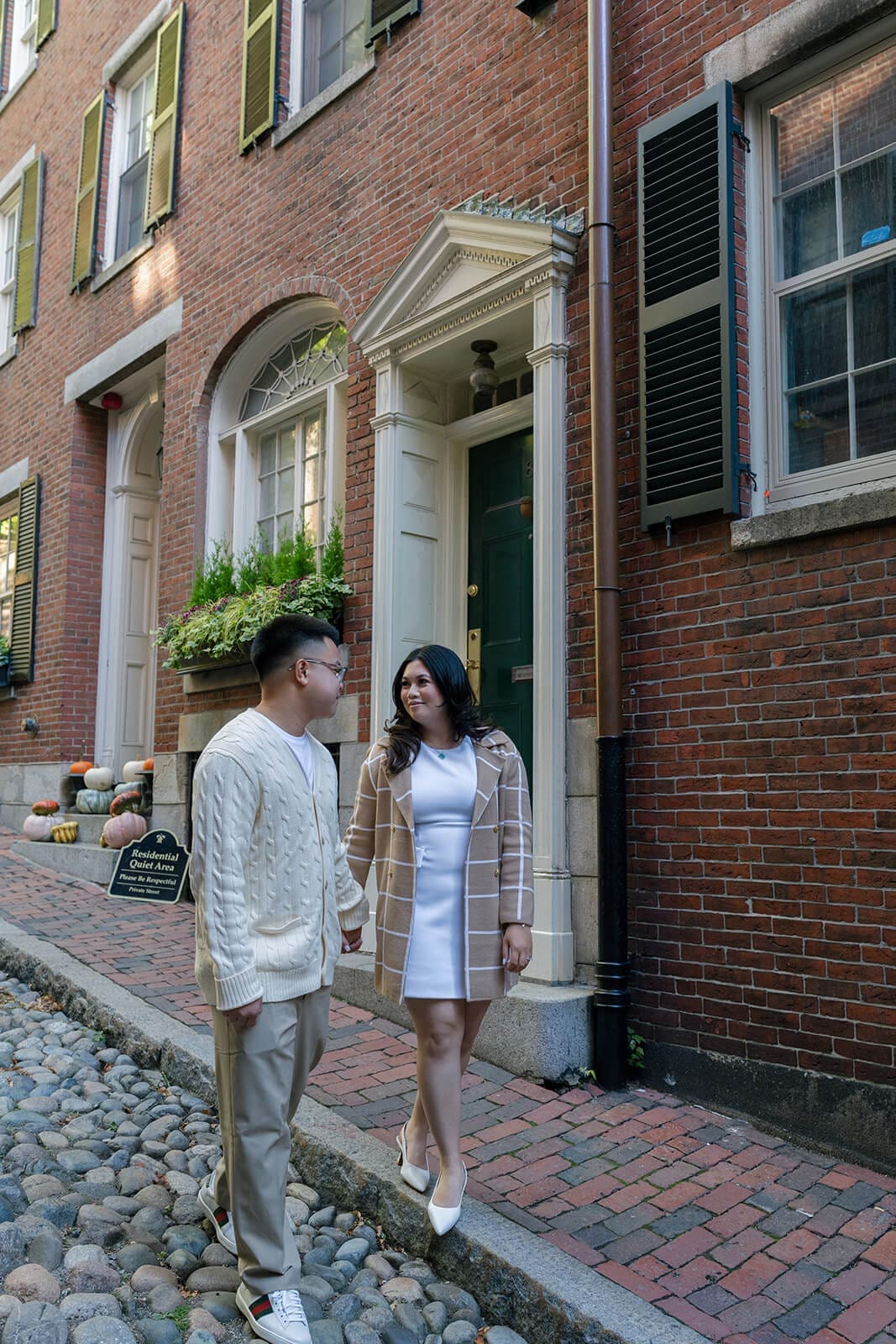 Couple walking together along a cobblestone sidewalk beside a historic brick home on Beacon Hill.