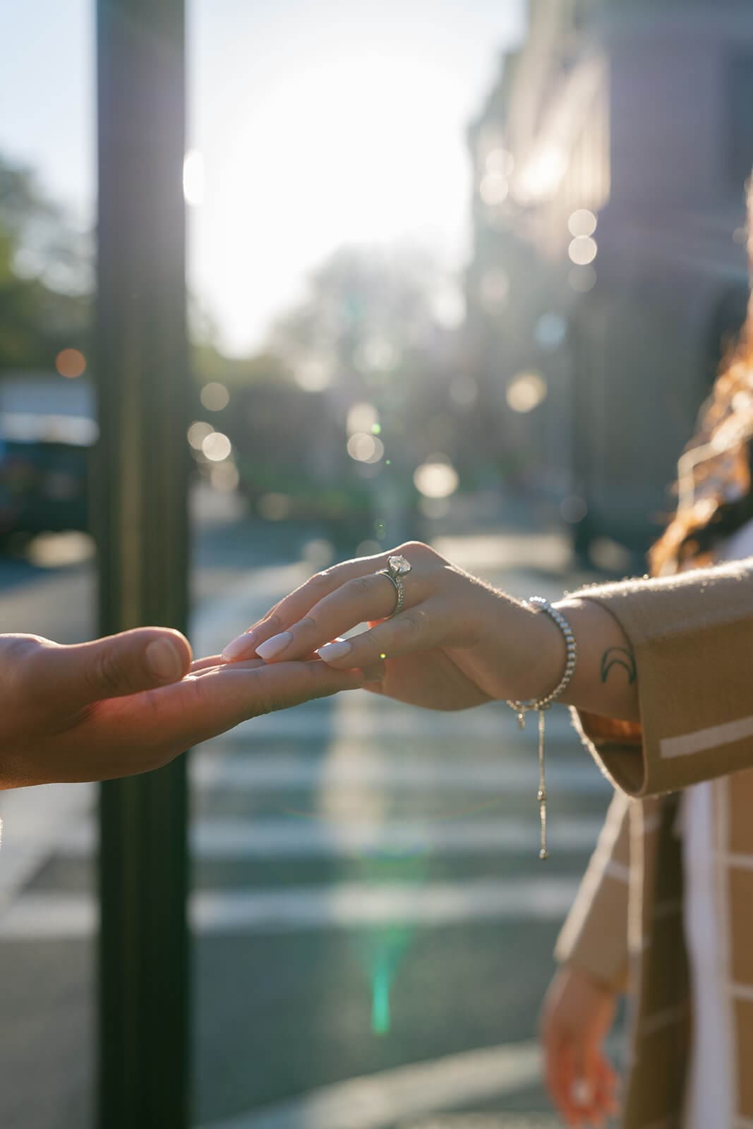 Close-up of a couple reaching for each other’s hands with an engagement ring visible in the afternoon sunlight.