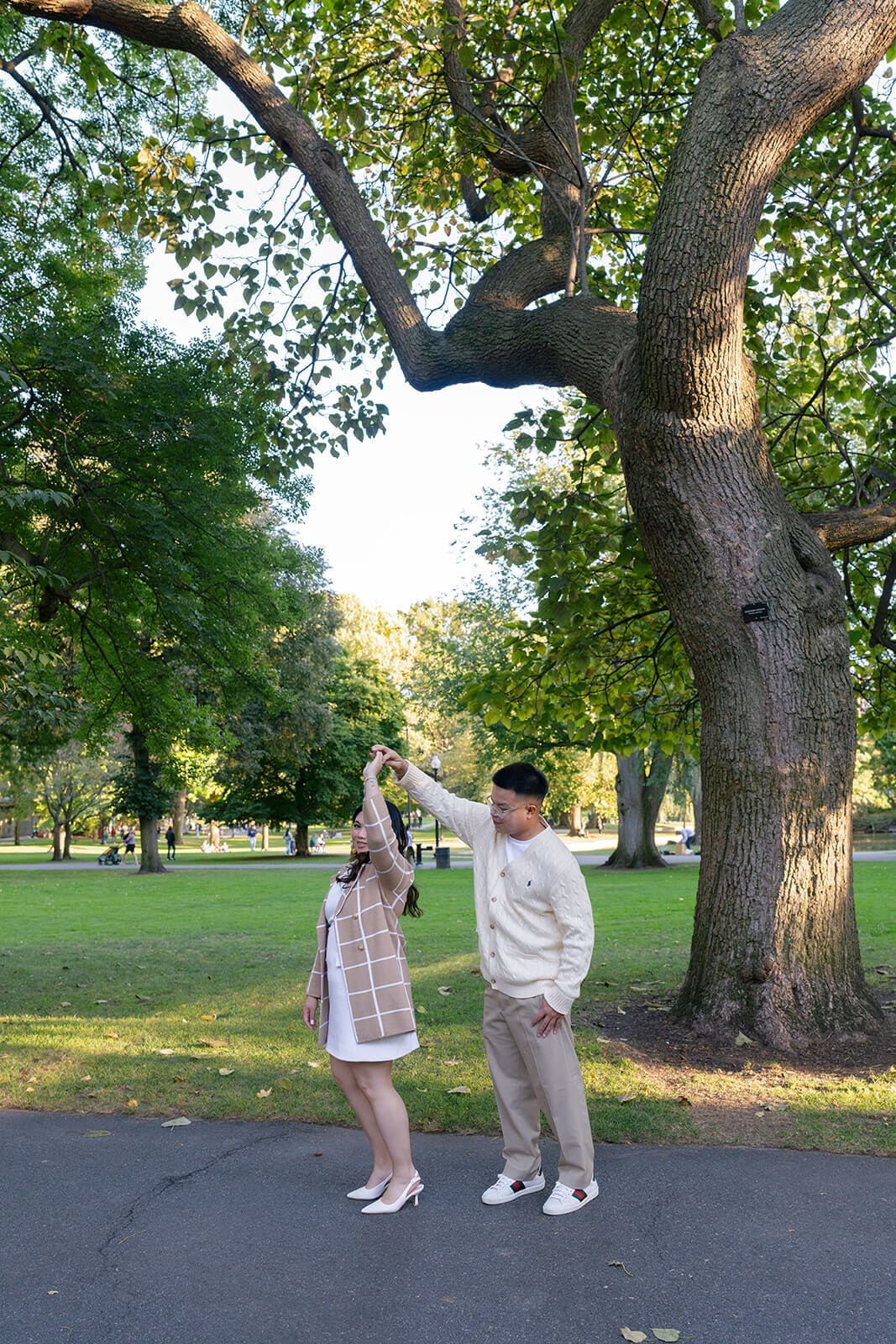 Couple playfully twirling beneath a large tree in Boston Public Garden during their engagement session.