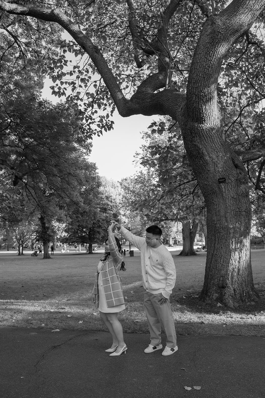 Black-and-white photograph of a man twirling his partner beneath a large tree in Boston Public Garden.