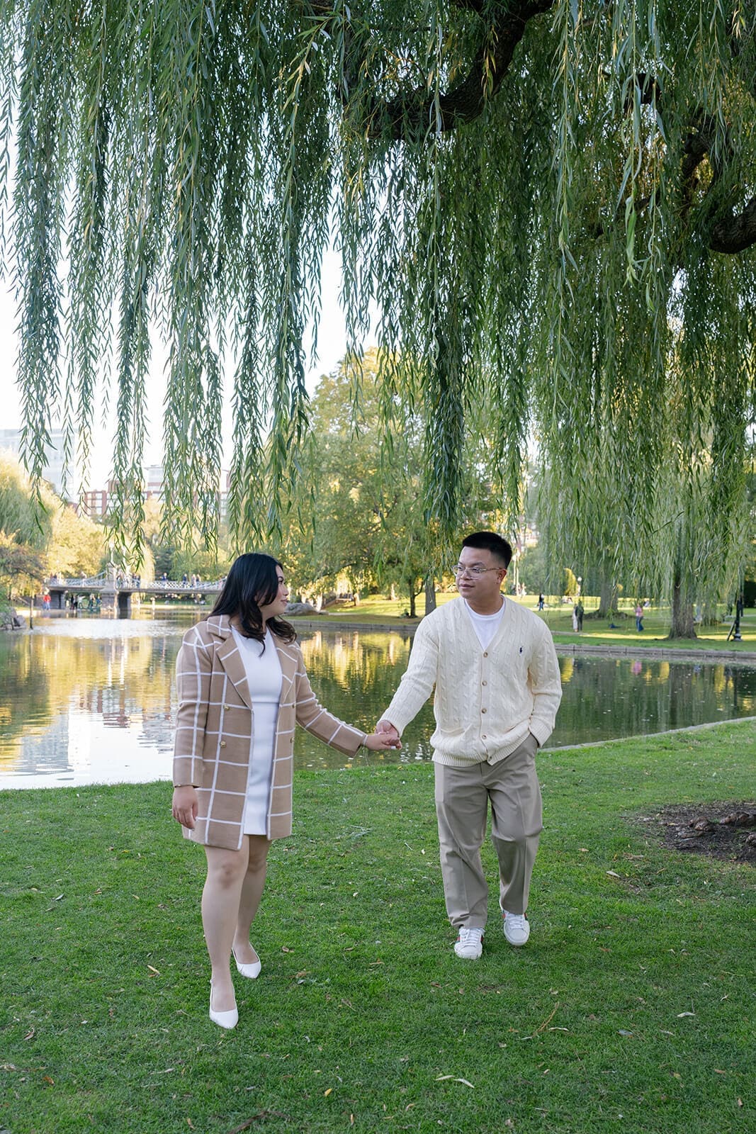 Couple walking hand in hand beside the pond and willow trees in Boston Public Garden.