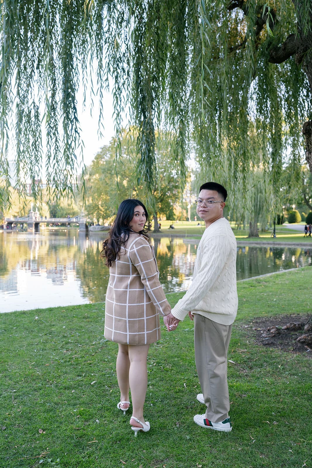 Couple holding hands beside the pond in Boston Public Garden and looking back toward the camera.