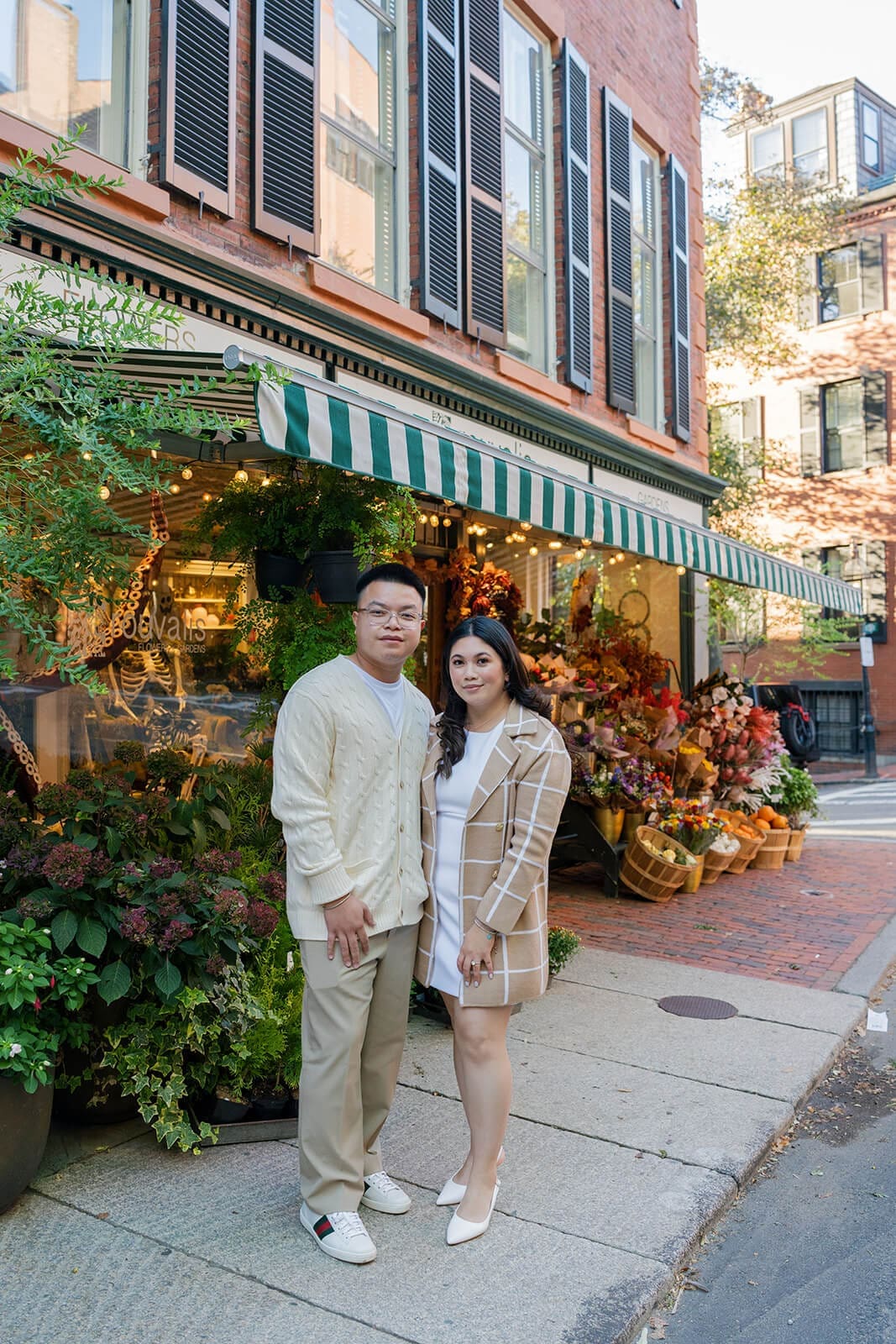 Couple standing together on a Beacon Hill sidewalk in front of a colorful flower shop with a green-and-white striped awning.