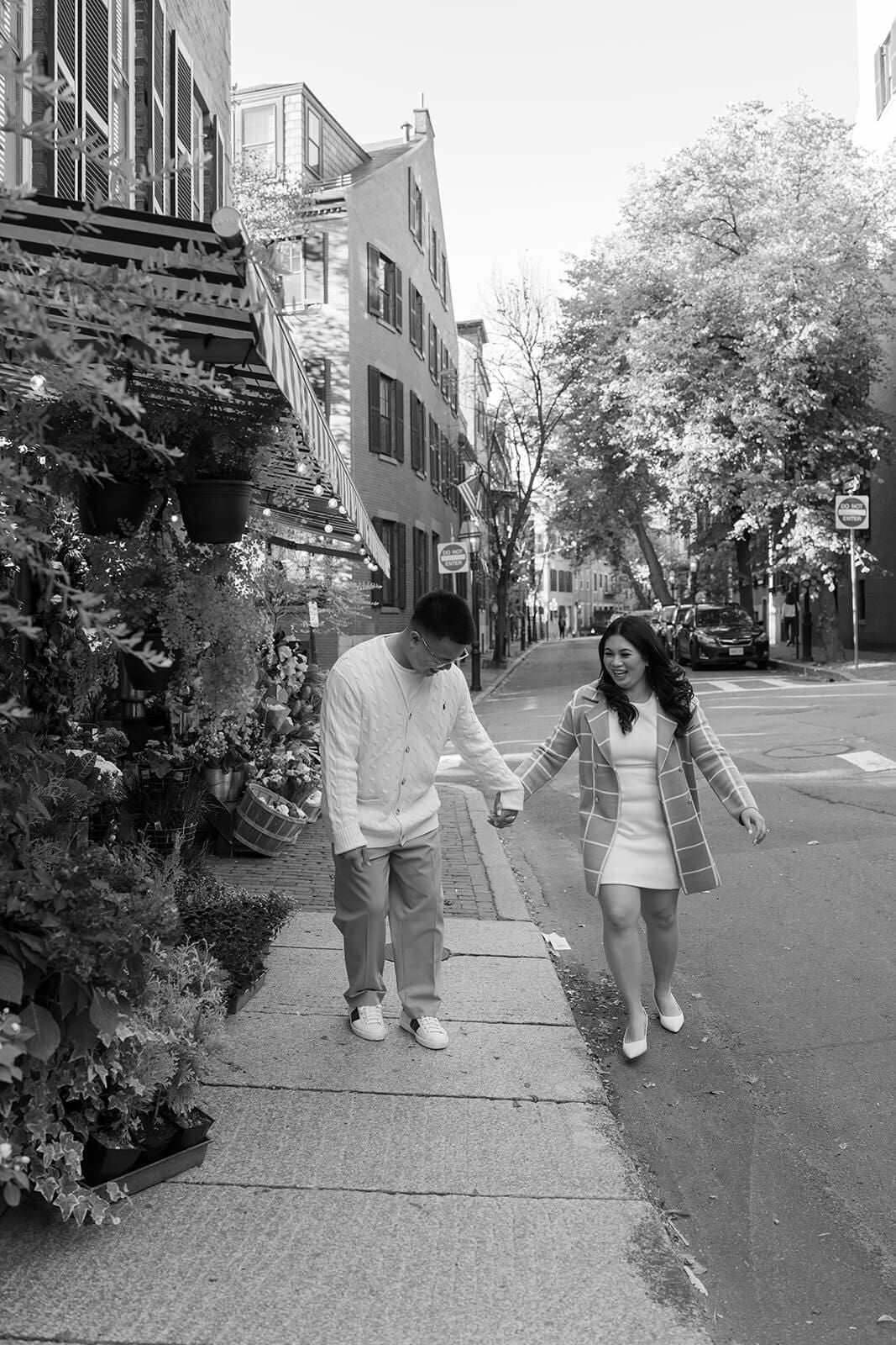 Black-and-white image of a couple holding hands and walking along a Beacon Hill sidewalk beside a flower shop.